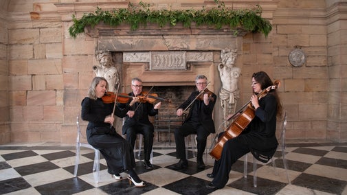 A string quartet playing by a grand fireplace